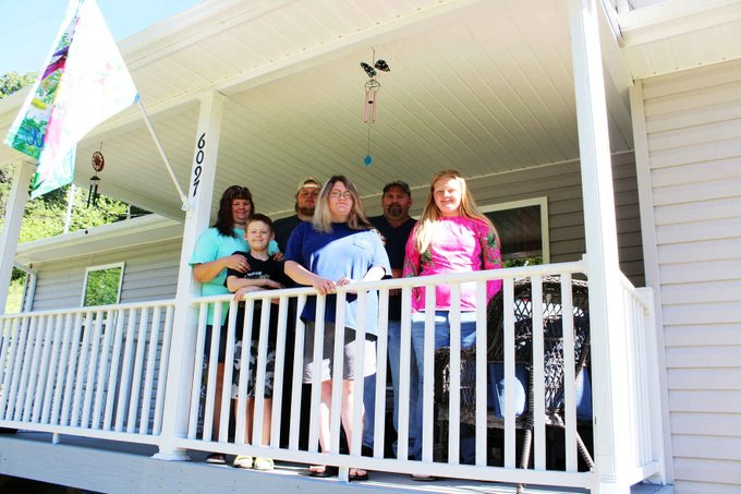 A family of six is standing outside on the front porch of a house.
