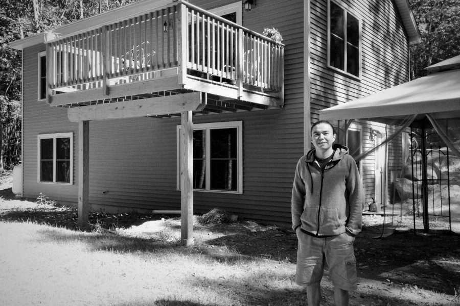 A young adult man is standing outside of a two-story home.