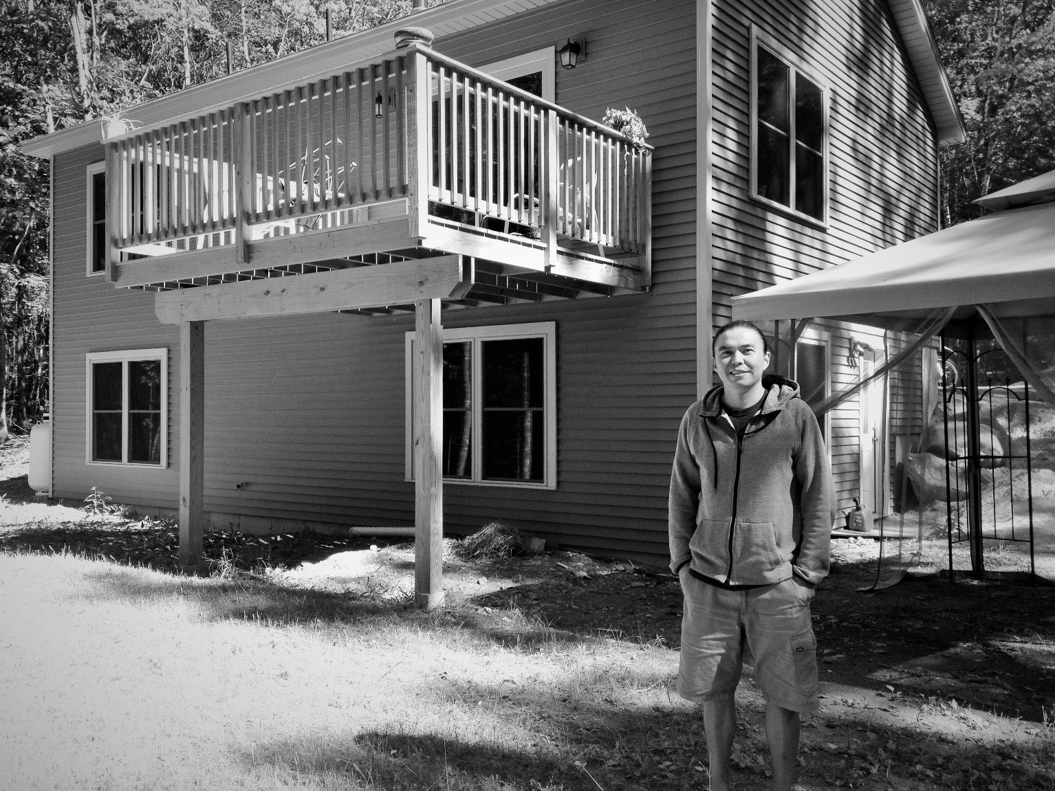 A young adult man is standing outside of a two-story home.