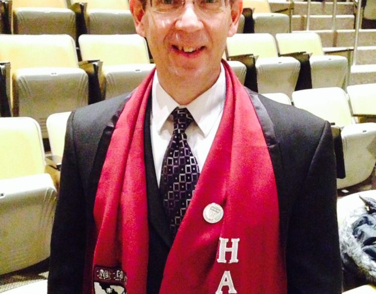 CEO Jim King is standing in an auditorium wearing a Harvard University scarf.