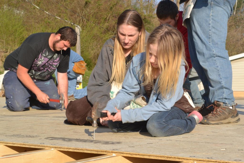 Mary Stamper and daughter hammering intro wood outside of a home construction site.