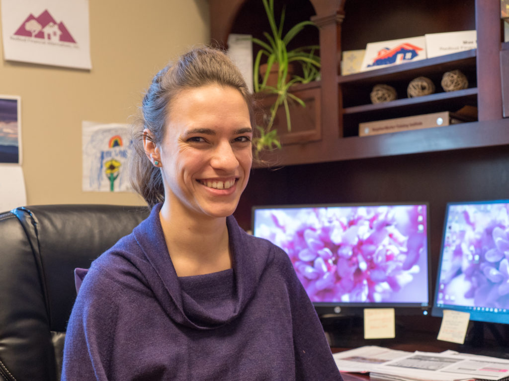 Mae Humiston, CDFI Manager, sitting at a desk with computer monitors behind her.