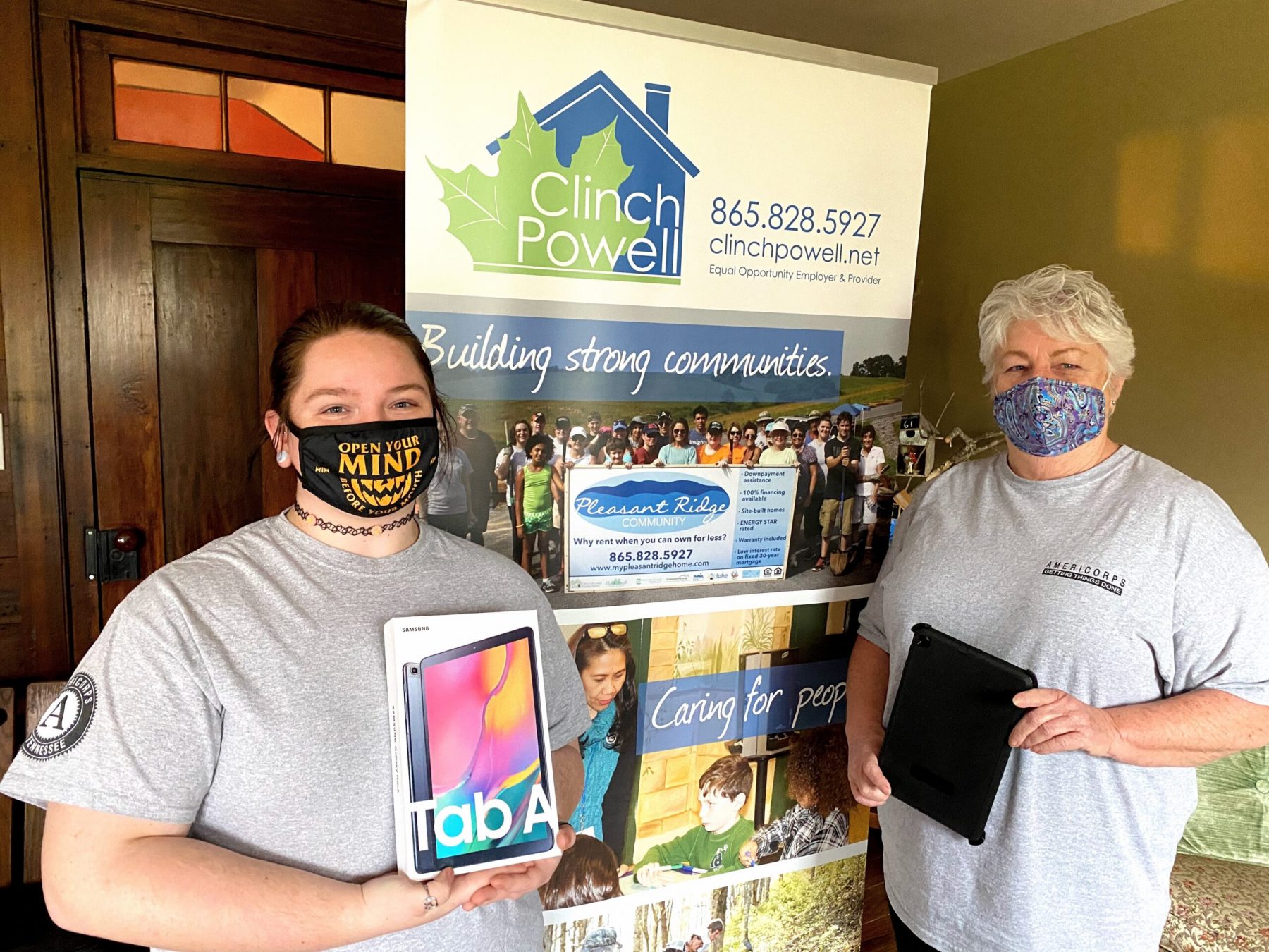 Two caucasian women with Covid-19 masks on are standing in front of a Clinch Powell pull up banner.