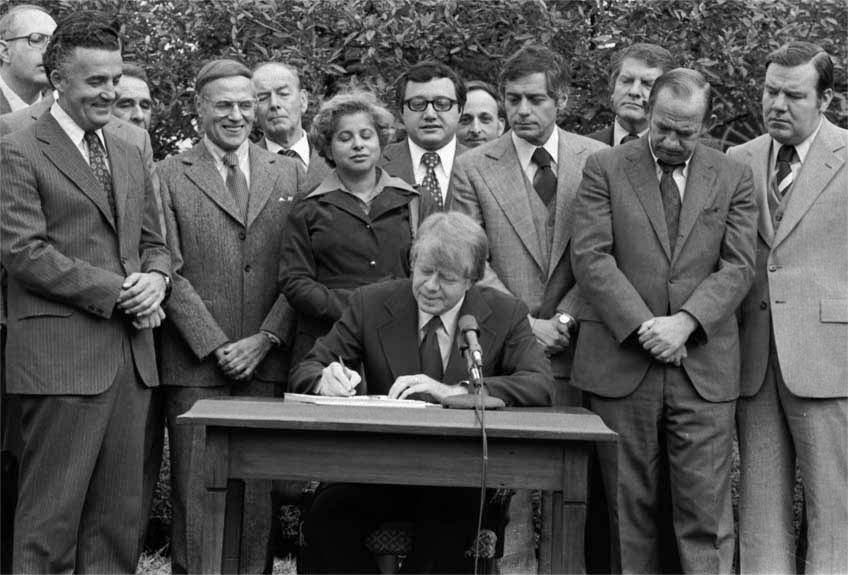 A group of people are standing around someone signing the Community Reinvestment Act at a table.