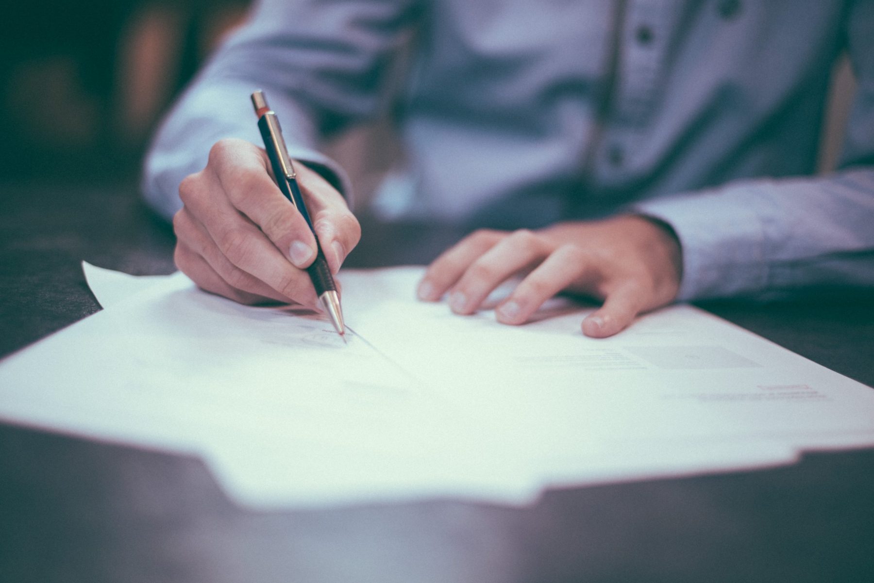 A person is holding a pen and signing paperwork.