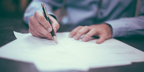 A person is holding a pen and signing paperwork.