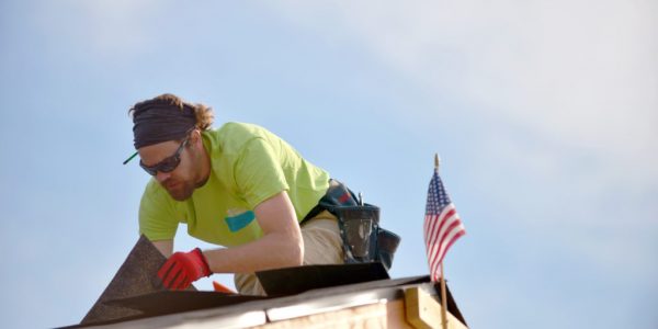 A caucasian man is placing roofing on a house.
