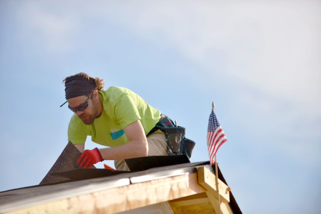 A caucasian man is placing roofing on a house.