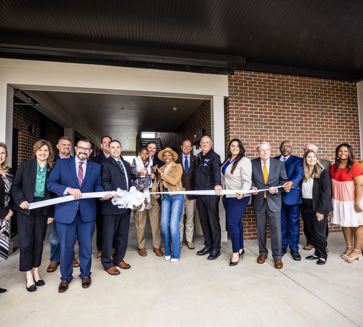 A group of people are smiling and standing outside of a building at a ribbon cutting event.