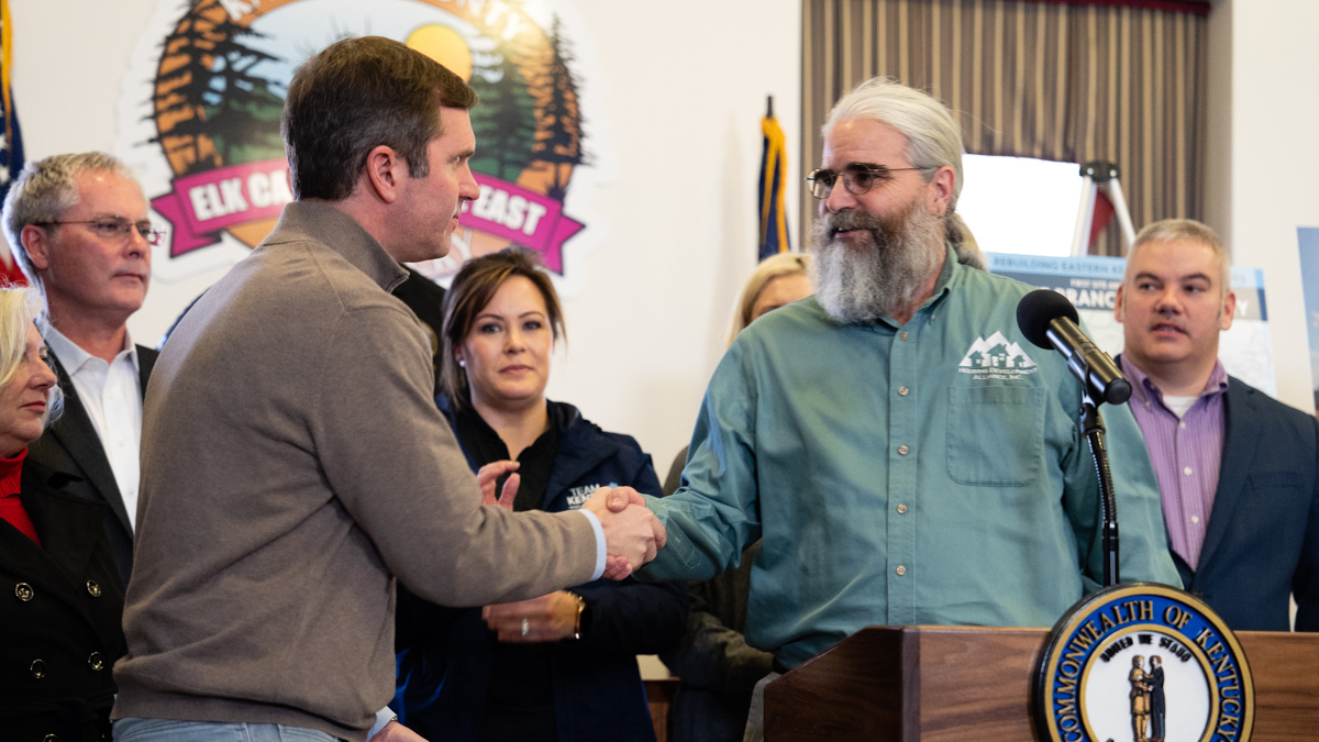 Scott Reynold's is shaking hands with a middle-aged adult man at a public event.