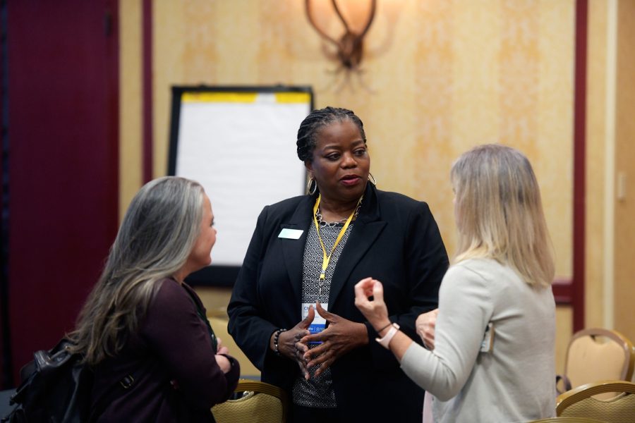 A group of Fahe members are in a conversation at an annual meeting event. There are tables and chairs behind them.
