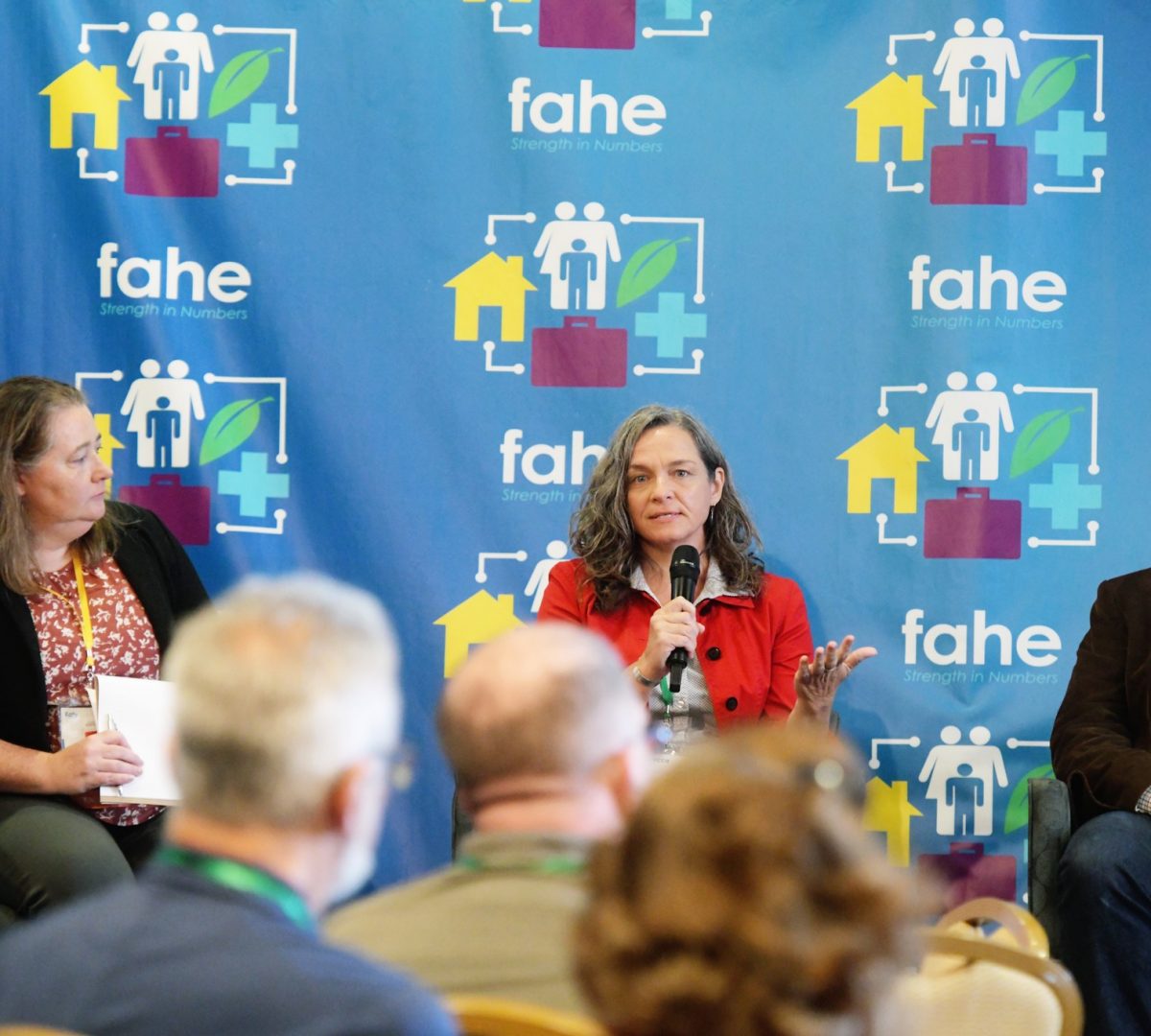 A caucasian woman is holding a microphone speaking at a Fahe annual event.