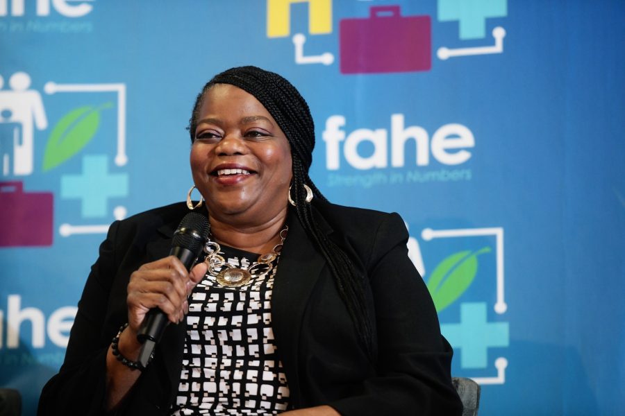 An African American woman is smiling and holding a microphone at an annual event. There is a Fahe step-and-repeat backdrop behind her.