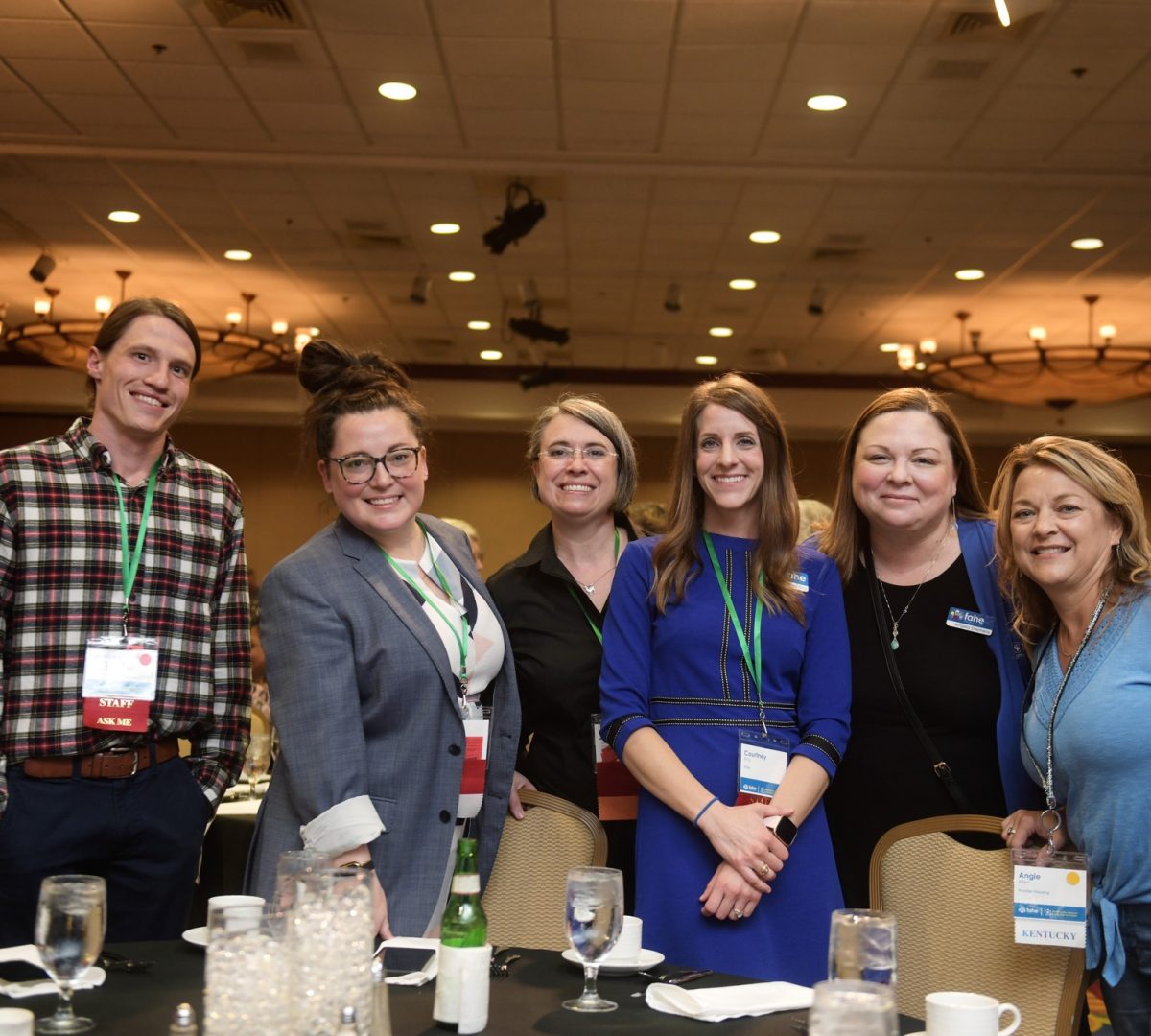 A group of six Fahe members are smiling and standing around a table in a ballroom at an annual event.