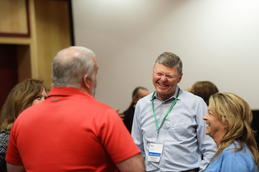 An older caucasian man is smiling laughing in conversation with other Fahe members.