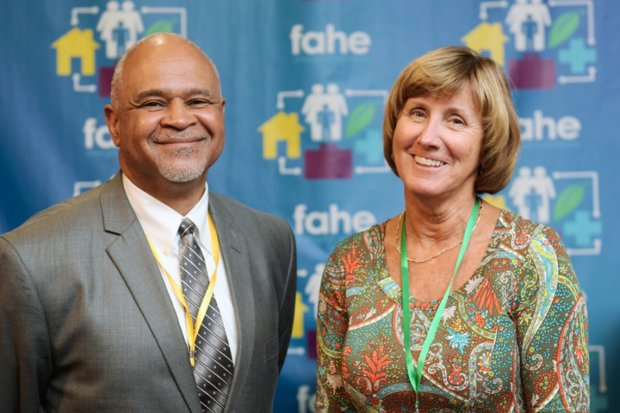 An older African American man is smiling standing next to a smiling middle-aged caucasian woman. There is a Fahe step-and-repeat backdrop behind them.